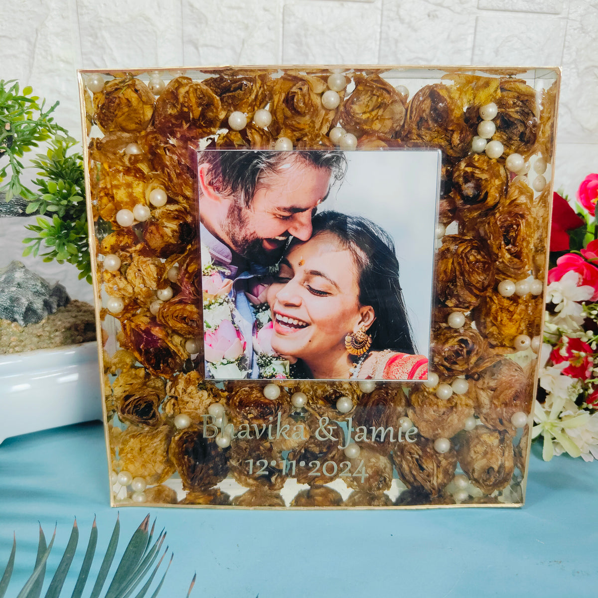 Clear square resin block packed with dried golden roses and pearls around a couple photo with names and date