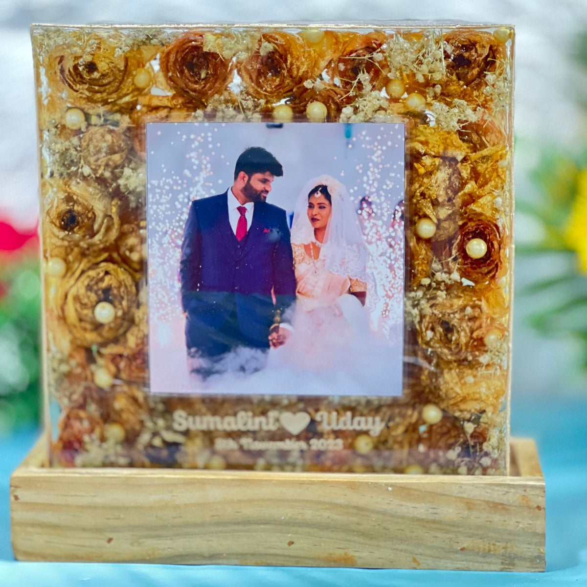 Square clear varmala block with golden flowers around a couple photo on a wooden LED base