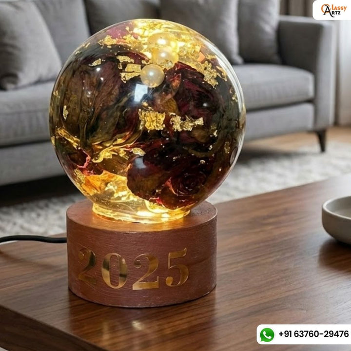 Clear resin globe lamp with red roses, pearls and gold flakes glowing on a brown wooden base with a date