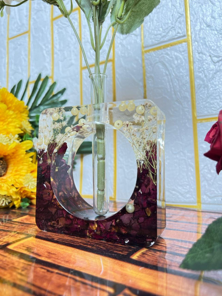 Square clear resin test tube planter with dark red rose petals, baby's breath and pearls on a wooden table