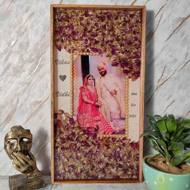 Tall rectangular wooden varmala frame with pink and maroon petals around a full length bridal couple photo